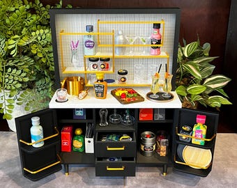 May include: A black bar cart with gold accents and glass shelves. The cart has a variety of bottles, glasses, and other bar accessories. The cart is open and the shelves are stocked with items. The cart has two doors on either side that are open.