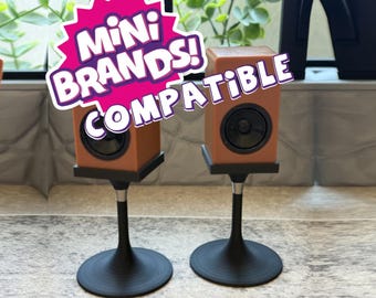 May include: Two brown miniature speakers with black circular drivers, each mounted on a black pedestal stand with a circular base. A white and pink graphic overlay with the text "MINI BRANDS! COMPATIBLE" is positioned over the speakers.