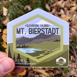 May include: A green and blue sticker with a mountain range illustration and the text "MT. BIERSTADT" and "ELEVATION: 14,060". The sticker also includes the text "EARLY LIGHT CREATIVE" and a logo with the text "EARLY LIGHT creative."