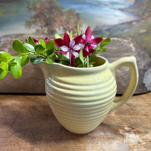 May include: A yellow ceramic jug with a ribbed design, filled with pink and white flowers and green leaves.