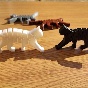 Peut inclure: Quatre figurines de chat articulées, chacune en plastique et peinte d'une couleur différente : blanc, gris, marron et noir. Les chats sont en position de marche.