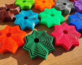 Puede incluir: Un conjunto de nueve cortadores de galletas con forma de estrella en varios colores, incluyendo rojo, naranja, verde, azul, morado y marrón. Los cortadores están superpuestos para crear un efecto multidimensional.
