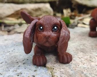 May include: A small brown puppy figurine with large ears and big brown eyes. The figurine is made of a textured material and has a realistic appearance.