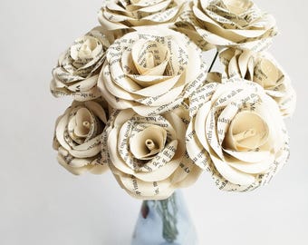 Puede incluir: Un ramo de rosas de papel de color crema hechas con páginas de libros, dispuestas en un jarrón azul.