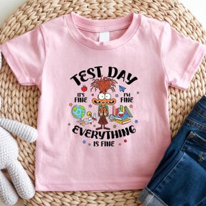 May include: Pink toddler t-shirt with a colorful graphic that reads "Test Day." The graphic features a cartoon character with books, a globe, and the words "It's Fine, I'm Fine, Everything is Fine."