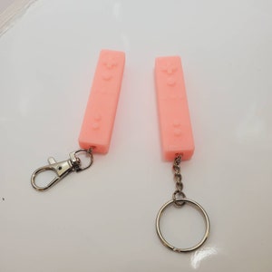 May include: Two pink silicone keychain charms shaped like a video game controller. One charm has a silver split ring and a silver lobster clasp. The other charm has a silver chain and a silver split ring.