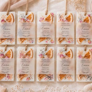 Personalized burnt orange soy wax sachet favors featuring dried orange slices, handmade soy wax air fresheners and custom vellum labels with names and dates. Elegant wedding favors, bridal shower favors, baby shower gifts, engagement party favors and wedding guest favors. Neutral boho decor with natural botanicals and premium fragrance oils. Perfect for wedding welcome bags, bridesmaid gifts, bridal events and special celebrations.