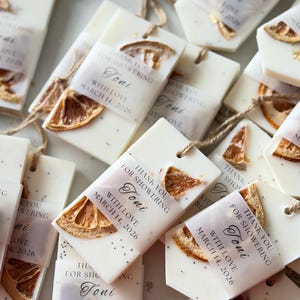 Personalized burnt orange soy wax sachet favors featuring dried orange slices, handmade soy wax air fresheners and custom vellum labels with names and dates. Elegant wedding favors, bridal shower favors, baby shower gifts, engagement party favors and wedding guest favors. Neutral boho decor with natural botanicals and premium fragrance oils. Perfect for wedding welcome bags, bridesmaid gifts, bridal events and special celebrations.