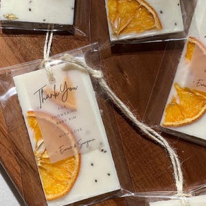 Personalized burnt orange soy wax sachet favors featuring dried orange slices, handmade soy wax air fresheners and custom vellum labels with names and dates. Elegant wedding favors, bridal shower favors, baby shower gifts, engagement party favors and wedding guest favors. Neutral boho decor with natural botanicals and premium fragrance oils. Perfect for wedding welcome bags, bridesmaid gifts, bridal events and special celebrations.