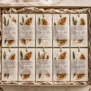 Personalized burnt orange soy wax sachet favors featuring dried orange slices, handmade soy wax air fresheners and custom vellum labels with names and dates. Elegant wedding favors, bridal shower favors, baby shower gifts, engagement party favors and wedding guest favors. Neutral boho decor with natural botanicals and premium fragrance oils. Perfect for wedding welcome bags, bridesmaid gifts, bridal events and special celebrations.