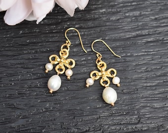 Peut inclure: Boucles d'oreilles en or avec un délicat motif floral et des accents de perles blanches.