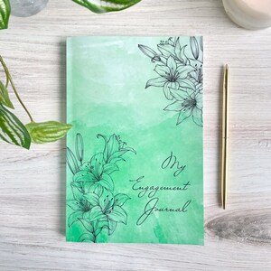 May include: A green journal with a watercolor background and black line drawings of lilies. The text "My Engagement Journal" is written in black cursive.