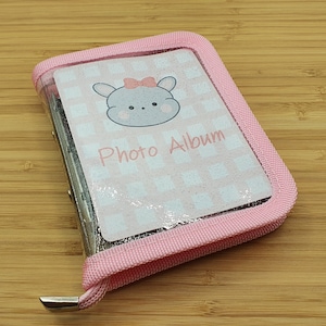 Könnte beinhalten: Ein rosa Fotoalbum mit einer durchsichtigen Plastikhülle, auf der ein Comic-Kaninchen mit Schleife und dem Text "Photo Album" abgebildet ist.