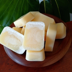May include: A collection of pale yellow, rectangular wax melts piled together. Each piece has a smooth, solid texture with a slightly powdery, matte finish on the top surface. The wax blocks are uniform in shape and colour, stacked in a cluster.