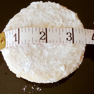 Puede incluir: Una galleta redonda blanca espolvoreada con az&uacute;car glas, medida con una cinta m&eacute;trica que muestra 7,6 cm de di&aacute;metro.