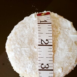 Puede incluir: Una galleta redonda blanca con az&uacute;car en polvo en la parte superior, medida con una cinta m&eacute;trica que indica 1, 2 y 3 pulgadas.