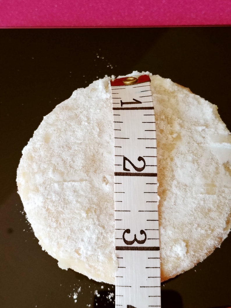 Puede incluir: Una galleta redonda blanca con az&uacute;car en polvo en la parte superior, medida con una cinta m&eacute;trica que indica 1, 2 y 3 pulgadas.