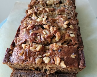 Può includere: Un pane alle banane con noci, affettato e pronto per essere mangiato. Il pane è di colore marrone chiaro e ha una crosta leggermente croccante. Le noci sono distribuite uniformemente in tutto il pane.