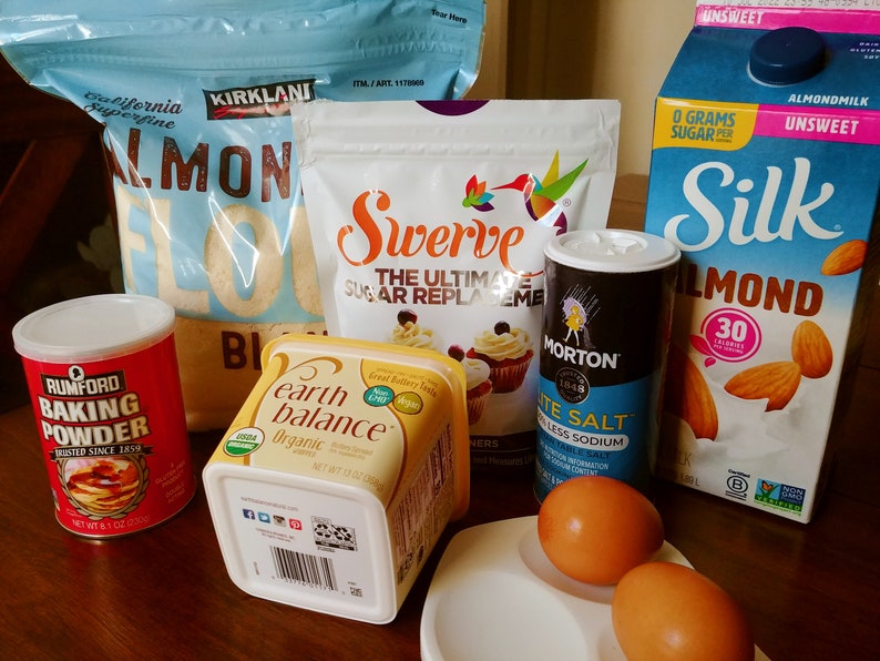 Puede incluir: Una colecci&oacute;n de ingredientes para hornear que incluye harina de almendras, polvo para hornear, mantequilla, sustituto del az&uacute;car, sal, leche de almendras y huevos.