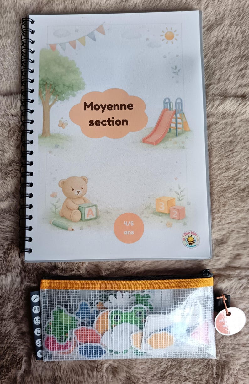 K&ouml;nnte beinhalten: Ein Spiralbuch mit dem Text "Moyenne section" und "4/5 ans" auf dem Cover, mit Illustrationen eines Spielplatzes, eines Teddyb&auml;ren und Bl&ouml;cken. Ein durchsichtiges Federm&auml;ppchen mit bunten Formen befindet sich darunter.