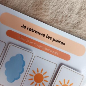 K&ouml;nnte beinhalten: Ein Kinderspiel mit dem Text "Je retrouve les paires" und "Associe les images identiques". Das Spiel zeigt Karten mit Illustrationen einer blauen Wolke und einer orangefarbenen Sonne. Der Hintergrund ist eine hellbraune, strukturierte Oberfl&auml;che.