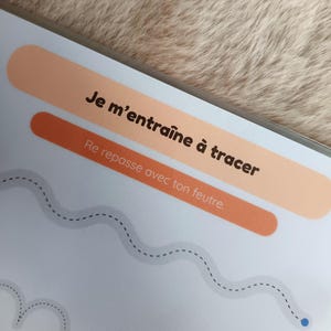 K&ouml;nnte beinhalten: Eine Seite aus einem Kinder-Aktivit&auml;tsbuch mit dem Text "Je m'entra&icirc;ne &agrave; tracer" und "Re repasse avec ton feutre". Die Seite hat einen hellblauen Hintergrund mit einer gepunkteten Linie zum Nachzeichnen. Zwei orangefarbene und pfirsichfarbene Rechtecke befinden sich oben.