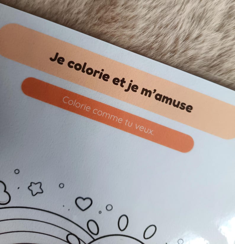 K&ouml;nnte beinhalten: Eine hellblaue Malbuchseite mit dem Text "Je colorie et je m'amuse" und "Colorie comme tu veux" in Schwarz. Die Seite hat eine Zeichnung eines Regenbogens, Herzen und Sterne.