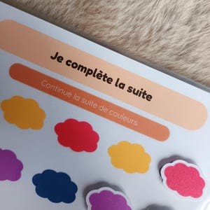 K&ouml;nnte beinhalten: Nahaufnahme einer Lernaktivit&auml;t mit dem Text "Je compl&egrave;te la suite" und "Continue la suite de couleurs". Bunte wolkenf&ouml;rmige Magnete in Lila, Gelb, Rot und Blau sind sichtbar. Der Hintergrund ist hellbraun.