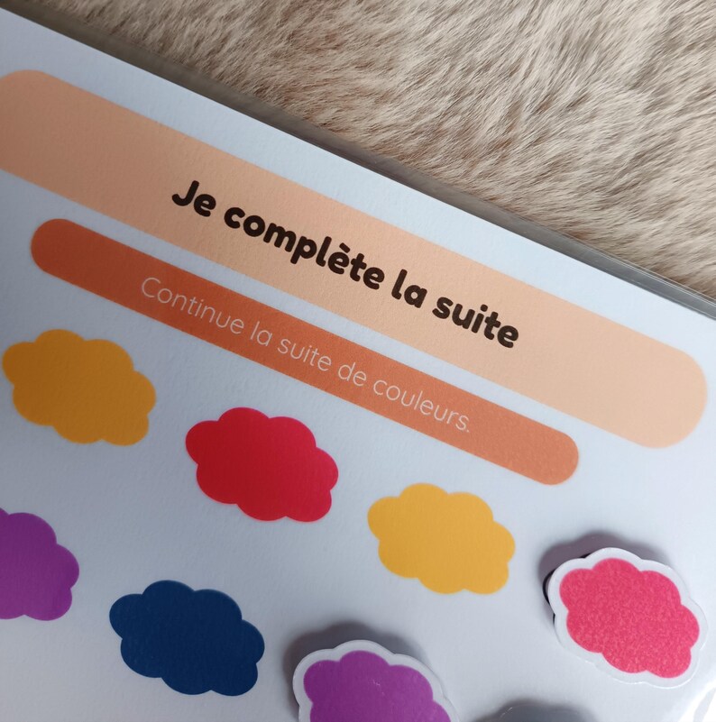 K&ouml;nnte beinhalten: Nahaufnahme einer Lernaktivit&auml;t mit dem Text "Je compl&egrave;te la suite" und "Continue la suite de couleurs". Bunte wolkenf&ouml;rmige Magnete in Lila, Gelb, Rot und Blau sind sichtbar. Der Hintergrund ist hellbraun.