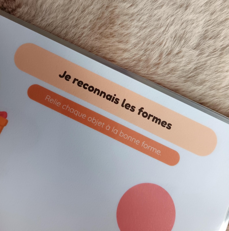K&ouml;nnte beinhalten: Eine Seite aus einem Kinderbuch mit dem Text "Je reconnais les formes" und "Relie chaque objet &agrave; la bonne forme" in schwarzer Schrift auf pfirsich- und orangefarbenen Bannern. Am unteren Rand der Seite ist ein rosa Kreis zu sehen.