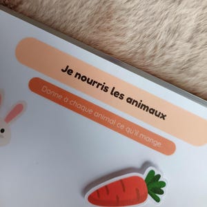 K&ouml;nnte beinhalten: Ein Kinder-Lehrbuch mit dem Text "Je nourris les animaux" und "Donne &agrave; chaque animal ce qu'il mange." Ein Karottenaufkleber und ein Cartoon-Kaninchen sind ebenfalls zu sehen.