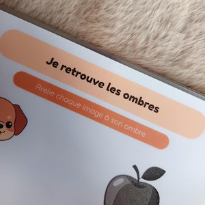 K&ouml;nnte beinhalten: Seite aus einem Kinder-Aktivit&auml;tsbuch mit dem Text "Je retrouve les ombres" und "Relie chaque image &agrave; son ombre". Die Seite zeigt einen Cartoon-Hund und einen schwarz-grauen Apfel.