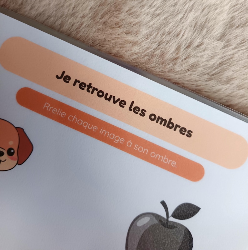 K&ouml;nnte beinhalten: Seite aus einem Kinder-Aktivit&auml;tsbuch mit dem Text "Je retrouve les ombres" und "Relie chaque image &agrave; son ombre". Die Seite zeigt einen Cartoon-Hund und einen schwarz-grauen Apfel.