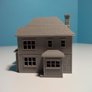 Puede incluir: Un modelo de casa de dos pisos, impreso en 3D, de color gris, con chimenea y porche. La casa tiene ventanas y un techo texturizado.