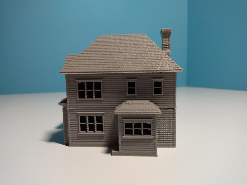 Puede incluir: Un modelo de casa de dos pisos, impreso en 3D, de color gris, con chimenea y porche. La casa tiene ventanas y un techo texturizado.