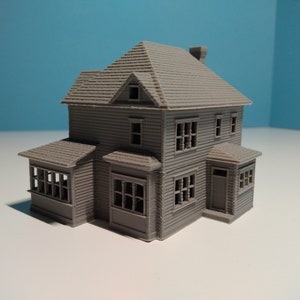 Puede incluir: Un modelo gris de una casa de dos pisos con un porche y una chimenea. La casa tiene varias ventanas y un techo de tejas.