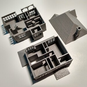 Puede incluir: Un modelo de casa impreso en 3D, separado en tres piezas: el techo, el primer piso y el segundo piso. El modelo es gris y muestra la distribuci&oacute;n interior de la casa.
