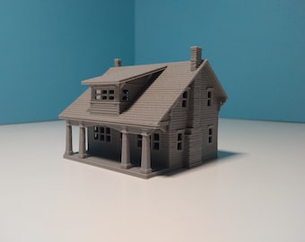 Op de afbeelding: Een grijs 3D-geprint model van een klein huis met een veranda en een tweede verdieping. Het huis heeft een zadeldak en meerdere ramen.