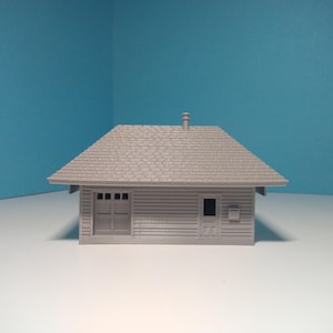 May include: A grey model of a small house with a shingled roof, a single door, and a window. The house has a chimney on the roof.