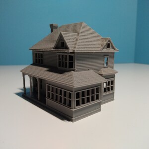 Puede incluir: Un modelo de casa de dos pisos impreso en 3D de color gris, con un porche y un techo a dos aguas.