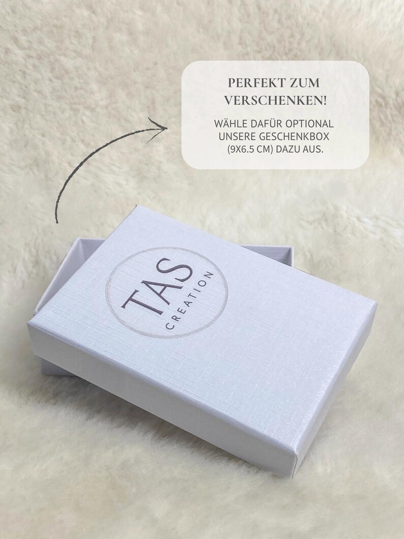 Pode incluir: Uma caixa de presente branca com o texto "TAS CREATION" em um logotipo circular. A caixa est&aacute; aberta, revelando seu interior. O texto na imagem diz "PERFEKT ZUM VERSCHENKEN! W&Auml;HLE DAF&Uuml;R OPTIONAL UNSERE GESCHENKBOX (9x6.5 cm) DAZU AUS."