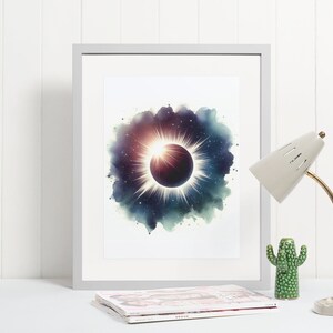 May include: A framed watercolour print of a solar eclipse with a dark blue, purple, and green background. The eclipse is surrounded by a white halo and stars. The print is in a white frame and is sitting on a white surface.