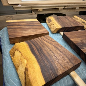 Könnte beinhalten: Vier Schneidebretter aus Holz mit natürlichen Holzmaserungen. Die Bretter sind in verschiedenen Größen und Formen, einige haben lebende Kanten. Die Bretter sind auf einer blauen gesteppten Oberfläche angeordnet.
