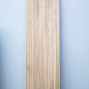 May include: A close-up of a light brown wood panel with vertical grooves. The wood has a natural grain pattern.