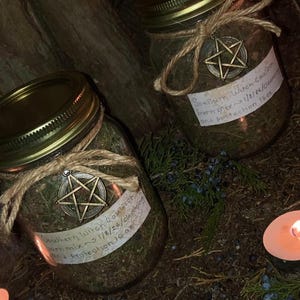 May include: Two glass jars with gold lids, filled with herbs and tied with twine. Each jar has a metal pentagram charm and a label that reads "Southern Witch Cauldron burn mix 1/8/26/cleaning and protection 16 oz."