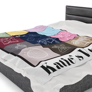 Puede incluir: Una manta de forro polar blanca con un dise&ntilde;o de patchwork colorido que presenta varias ilustraciones. La manta tiene un borde negro y el texto "Katie's Love" en letras negras.