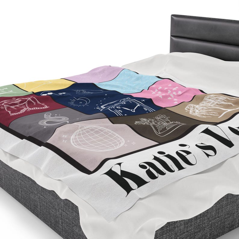 Puede incluir: Una manta de forro polar blanca con un dise&ntilde;o de patchwork colorido que presenta varias ilustraciones. La manta tiene un borde negro y el texto "Katie's Love" en letras negras.