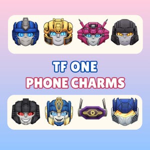 May include: A collection of cartoon-style phone charms featuring robot faces in various colors, including blue, gold, pink, and black. The text "TF ONE PHONE CHARMS" is displayed in blue and pink. The charms have detailed designs and glowing eyes.