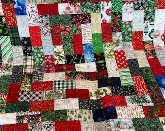 May include: A patchwork quilt featuring a variety of Christmas-themed fabrics. The quilt is composed of numerous squares in red, green, white, and blue, with patterns including candy canes, snowflakes, and holiday ornaments. The quilt is a festive and cozy home decor item.