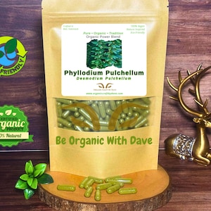 May include: A kraft paper bag with a clear window, filled with green capsules. The label reads "Phyllodium Pulchellum." The bag is on a wooden surface with scattered capsules. Text on the bag says "Be Organic With Dave." Eco-friendly and organic product.